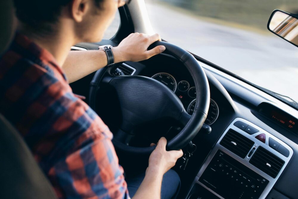 An over-the-shoulder view of a driver wearing a plaid shirt.